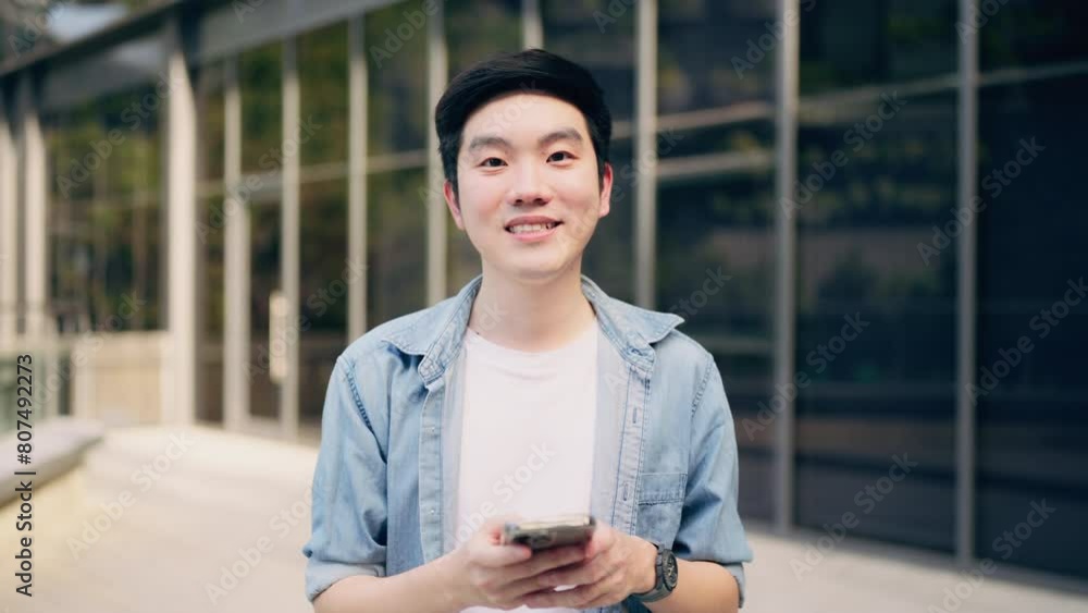 Young asian happy man standing use phone looking on camera and smiling Young asian happy man standing use phone looking on camera and smiling