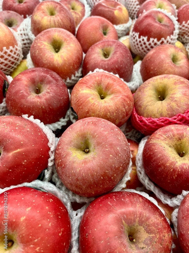 Sweet pinkish red fuji apple fruits wrapped in white plastic nets in market store stall display. Healthy natural food full of vitamins. Group of fruits isolated on full frame vertical ratio background