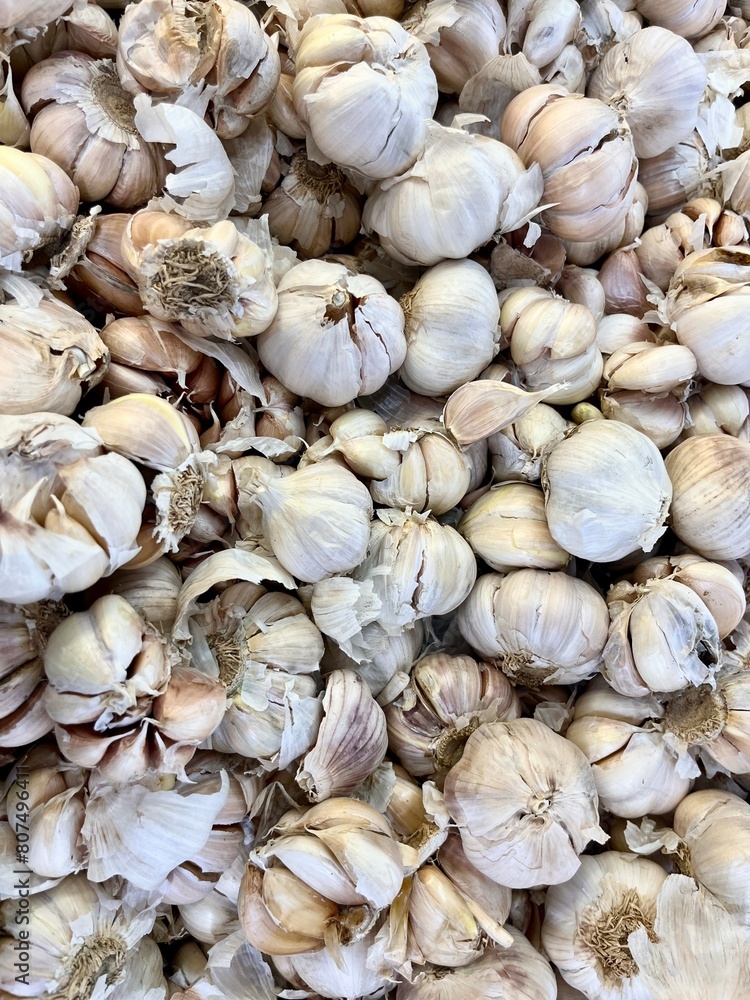 Groups of white garlic bulbs and pieces. Raw food cooking ingredients spice isolated on full frame vertical ratio background in market stall display. Groups of white garlic bulbs and pieces. Raw food cooking ingredients spice isolated on full frame vertical ratio background in market stall display.