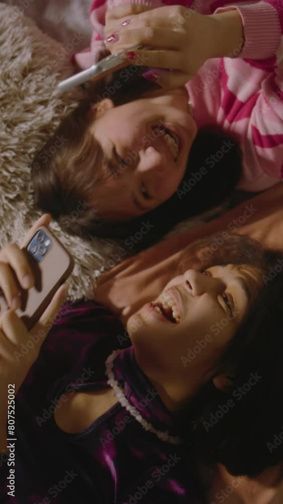 Two multiethnic best friends in the bedroom laugh and scroll through social media using mobile phone. Happy teenage girls spend leisure time at home lying on the bed. Besties having fun together. Two multiethnic best friends in the bedroom laugh and scroll through social media using mobile phone. Happy teenage girls spend leisure time at home lying on the bed. Besties having fun together.