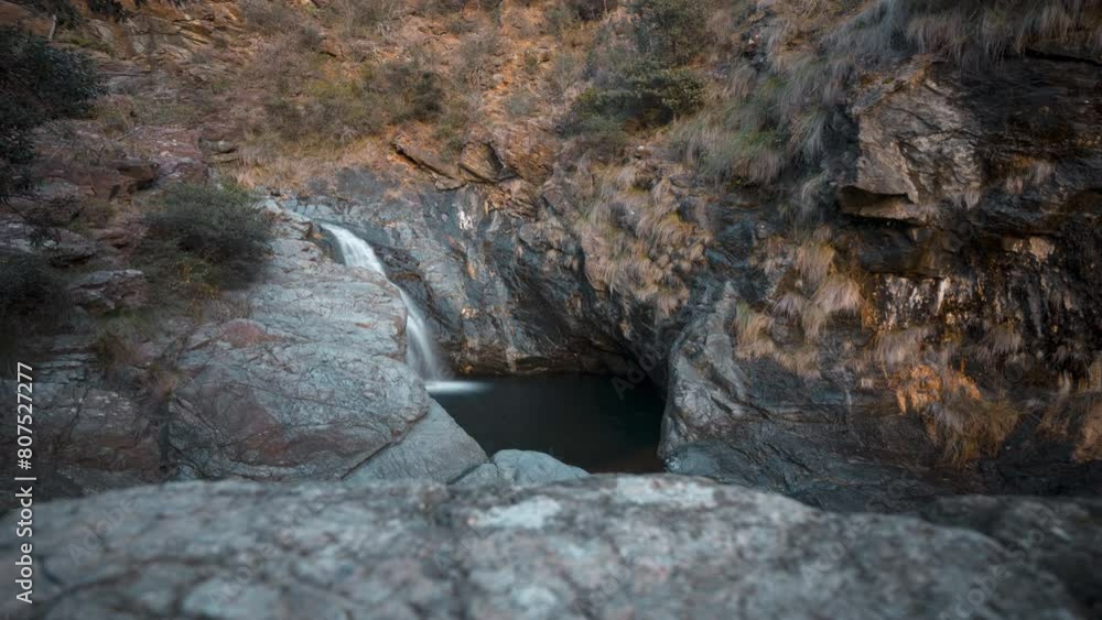 Golden hour timelapse of a serene waterfall cascading into a rocky pool surrounded by rugged cliffs Golden hour timelapse of a serene waterfall cascading into a rocky pool surrounded by rugged cliffs