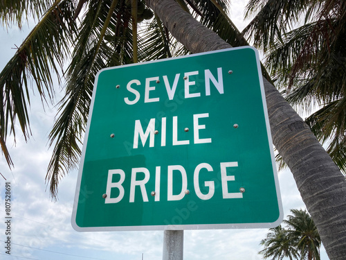 Seven Mile Bridge road sign, surrounded by palm leaves, at Overseas Highway in the Florida Keys
