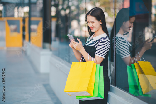 A woman is standing outside with a cell phone in her hand and two shopping bags