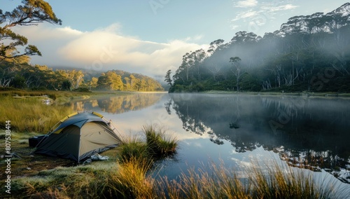 A tent pitched by a serene riverbank, the water reflecting the surrounding landscape.