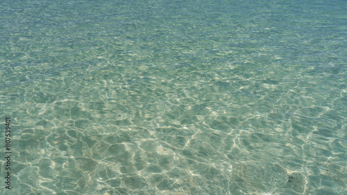 Crystal clear water. Close-up. Full screen. View from above. Circles from water droplets and glare are visible on the wavy shiny surface. The sandy bottom. Madagascar
