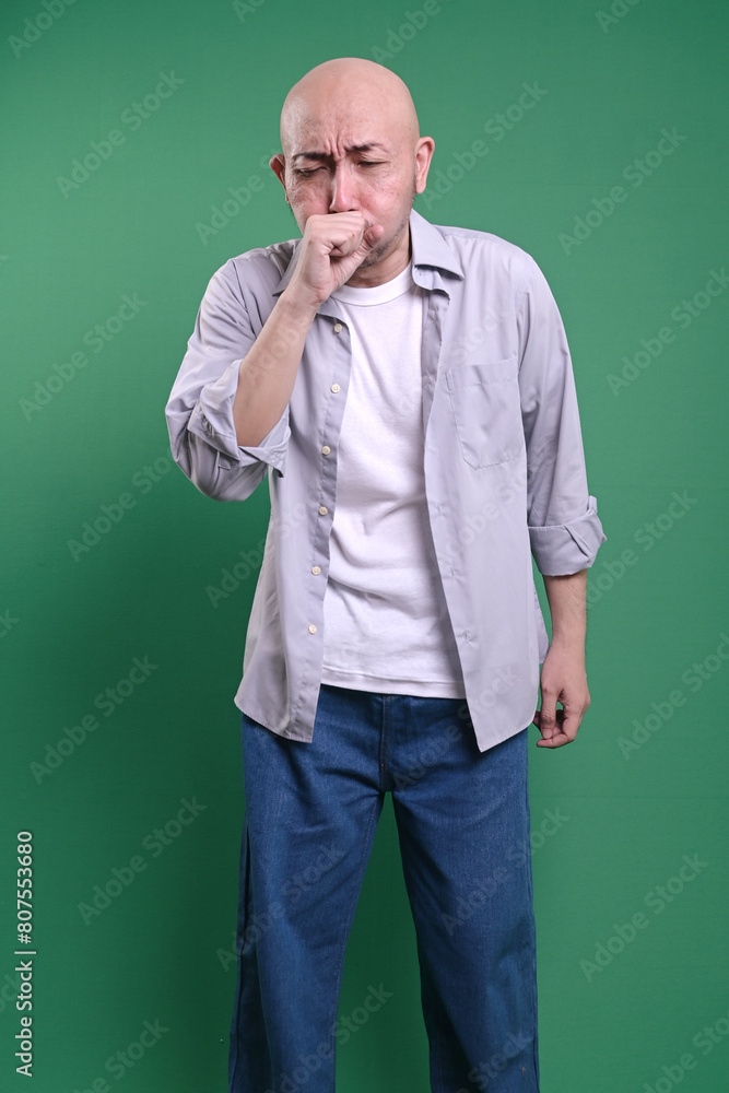 Asian bald man coughing into his fist on green background Asian bald man coughing into his fist on green background