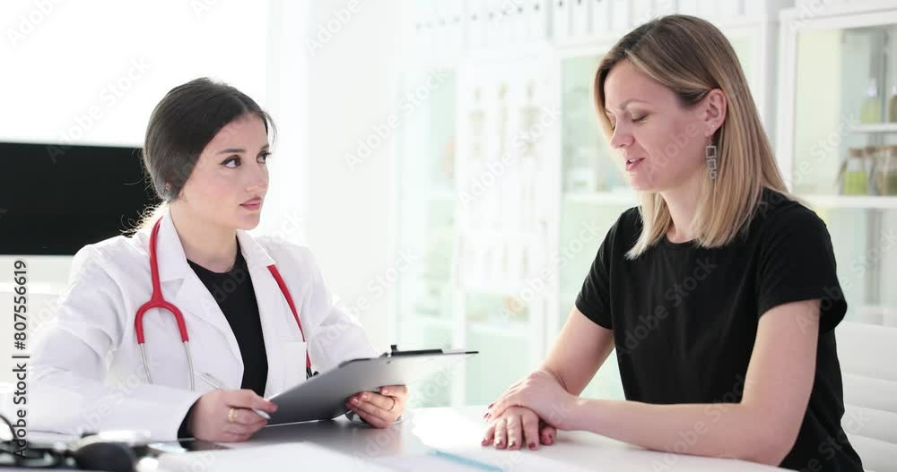 Woman sits at desk and discusses symptoms with doctor Woman sits at desk and discusses symptoms with doctor