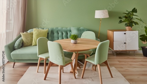 Mint color chairs at round wooden dining table in room with sofa and cabinet near green wall