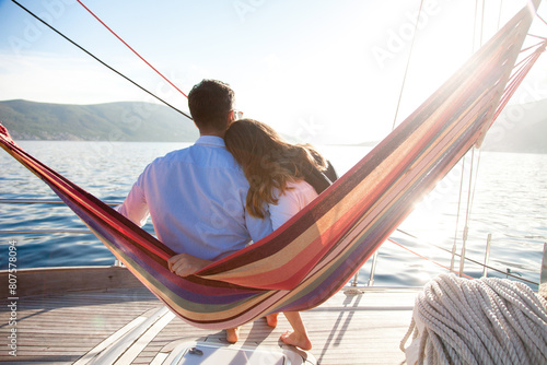 Couple in love relaxing in beach hammock on yacht at sea. Man and woman traveling, enjoying summer vacations, nature. Rest on holidays. Slow living, slowing down lifestyle moment photo
