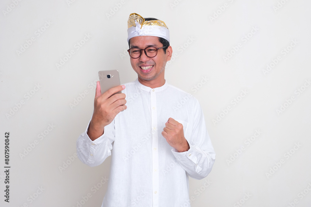 Balinese man clenched fist showing excited when looking to mobile phone that he hold Balinese man clenched fist showing excited when looking to mobile phone that he hold