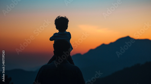  a heartwarming Father s Day unfolds against the majestic backdrop of mountain peaks. Silhouetted against the fading light son perched joyfully on his father s shoulders