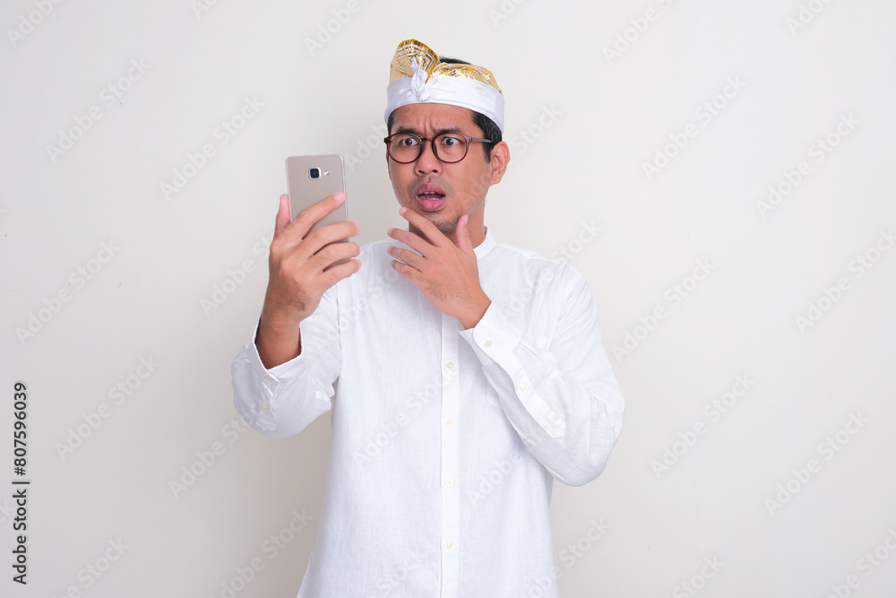 Balinese man looking to his mobile phone with shocked face expression Balinese man looking to his mobile phone with shocked face expression