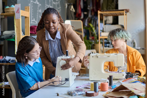 Portrait of Black young woman teaching girl with disability using sewing machines in vocational training class copy space