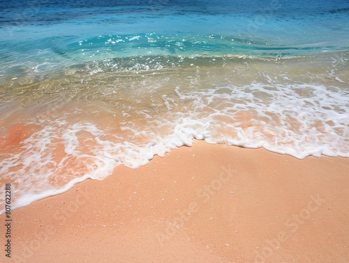 A sandy beach with a wave rolling towards the shore under a soft blue sky