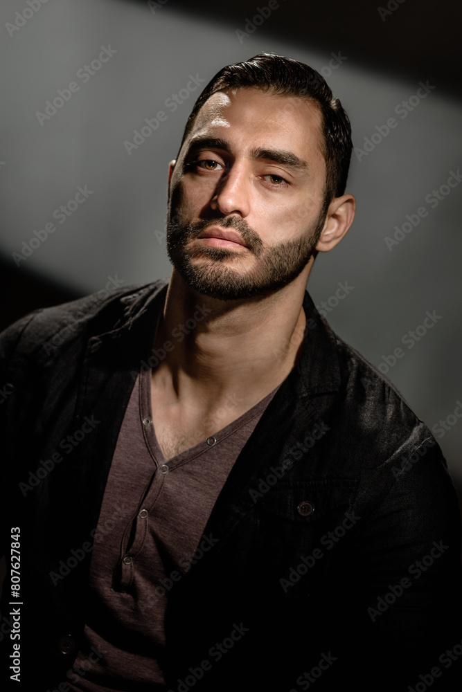 Obraz premium Portrait of young stylish brutal bearded man on dark studio background, Intense presence: A man's dark and dramatic portrait showcases brutal strength and a bold beard