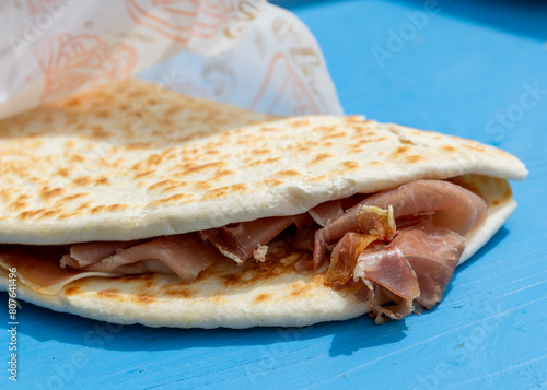 Tasty Piadina Romagnola Wrapped in generic, unbranded but decorated oily paper, authentic street food from the Riviera Romagnola region of Italy, with Prosciutto Crudo ham filling. 