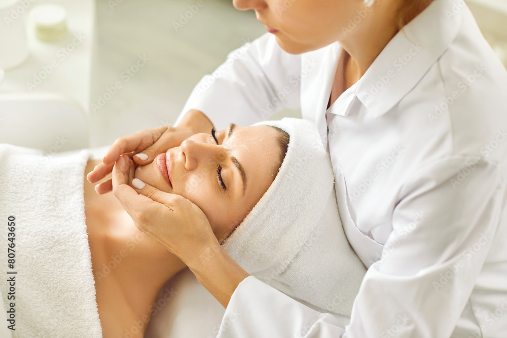 Portrait of pretty relaxed young woman lying with closed eyes having facial massage in spa salon. Female client enjoy receiving skin care procedure treatment. Wellness and beauty day concept. Portrait of pretty relaxed young woman lying with closed eyes having facial massage in spa salon. Female client enjoy receiving skin care procedure treatment. Wellness and beauty day concept.