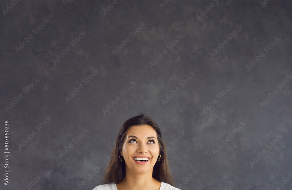 Smiling young Hispanic woman on black studio background look up at blank empty copy space. Happy millennial Latino female think recommend good sale offer or promotion discount deal. Copyspace. Smiling young Hispanic woman on black studio background look up at blank empty copy space. Happy millennial Latino female think recommend good sale offer or promotion discount deal. Copyspace.