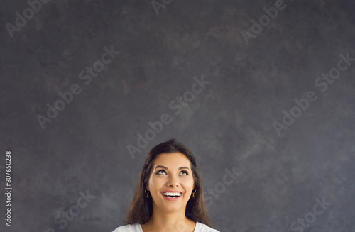 Smiling young Hispanic woman on black studio background look up at blank empty copy space. Happy millennial Latino female think recommend good sale offer or promotion discount deal. Copyspace. © Studio Romantic