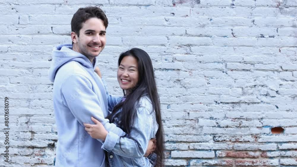 Young interracial couple kissing and embracing by a blue brick wall. Young interracial couple enjoying their date in the city. Young interracial couple kissing and embracing by a blue brick wall. Young interracial couple enjoying their date in the city.
