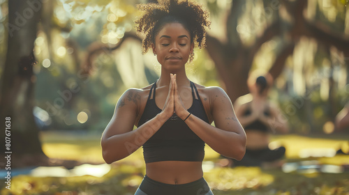 A young woman in a black sports bra and black leggings is sitting in a yoga pose with her eyes closed and her hands together in front of her chest photo
