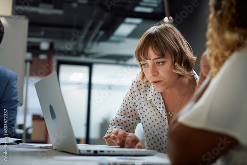 Three focused multiracial business people in businesswear using laptop at meeting in office