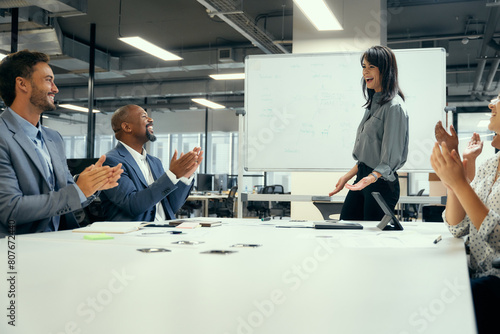 Five happy multiracial business people applauding around conference table in office