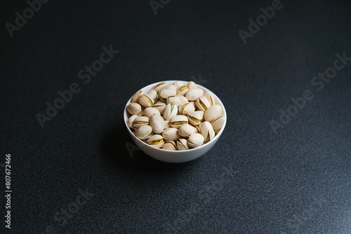 Flat lay of pistachio nuts in white bowl in a morning light and shadow from a window frame.