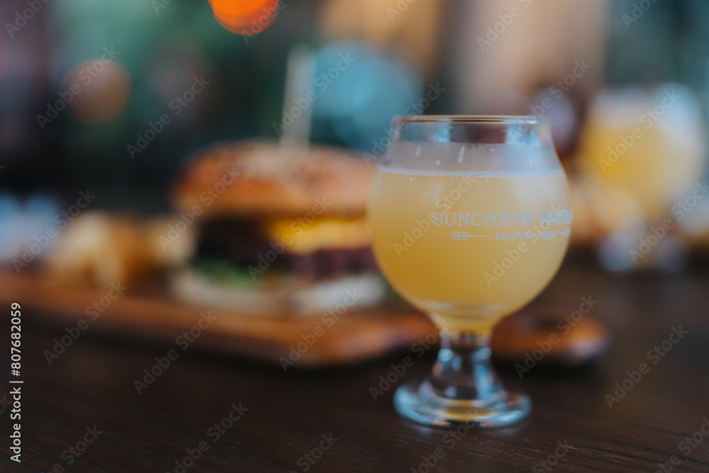 A glass of beer sits on a table next to a hamburger A glass of beer sits on a table next to a hamburger