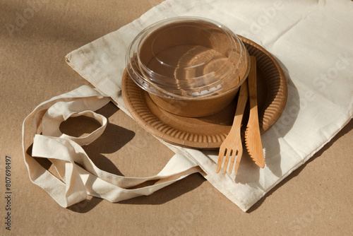 A set of paper utensils and wooden cutlery in fabric bag on a brown background. Eco friendly, zero waste concept. Top view