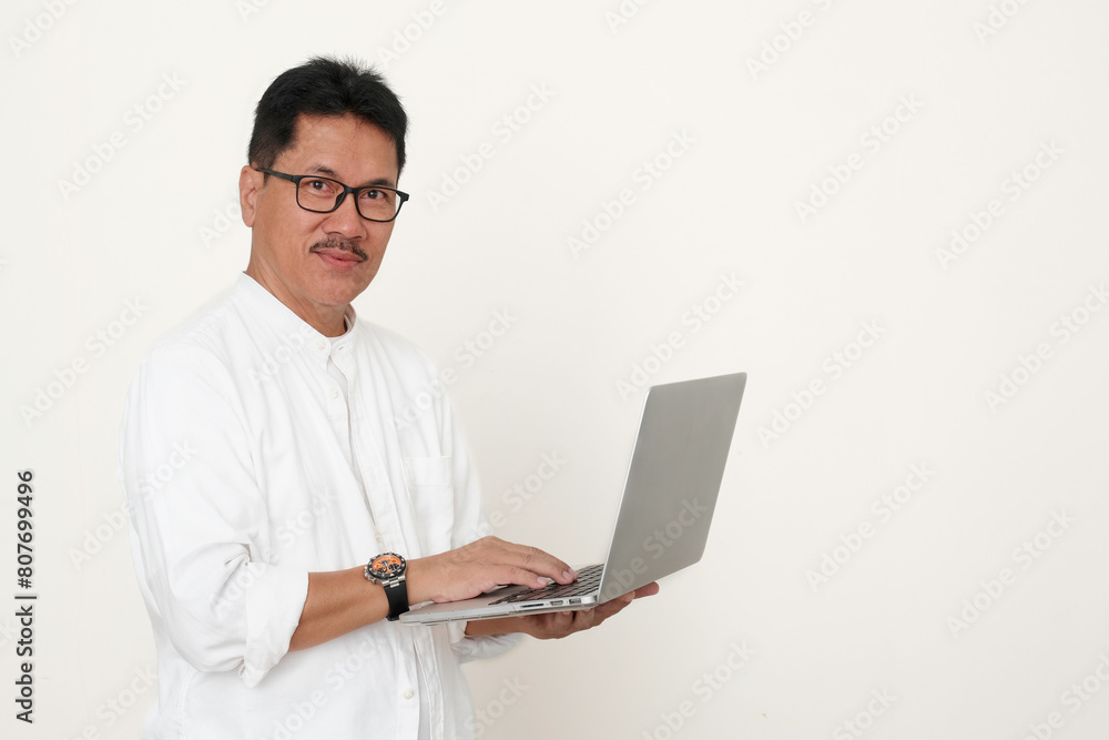 A man stands while working on his laptop; smile, friendly expression A man stands while working on his laptop; smile, friendly expression