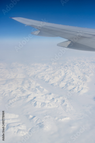 View from a flying airplane of snow-capped mountains under the wing of the airplane. Winter aerial landscape. Travel and aviation tourism in the Arctic. Flight on a passenger airliner. Polar region.