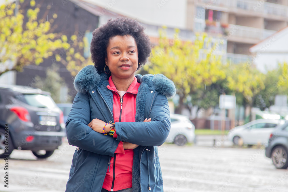 afro woman with crossed arms and winter jacket on the street