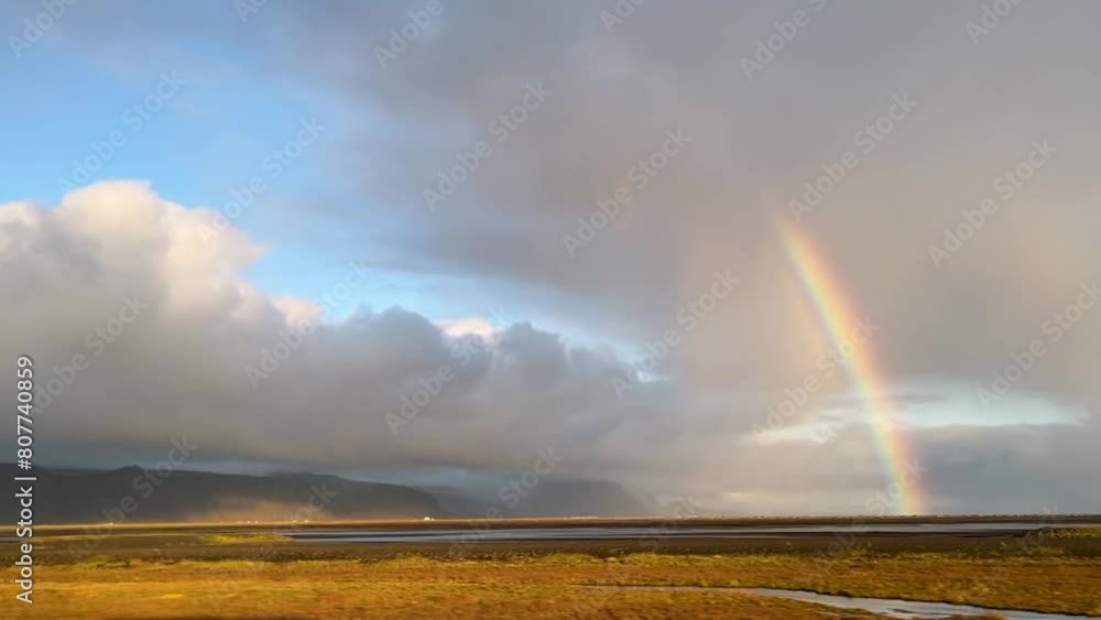 Magical landscape of Iceland with rainy clouds and rainbow, view from moving car Magical landscape of Iceland with rainy clouds and rainbow, view from moving car