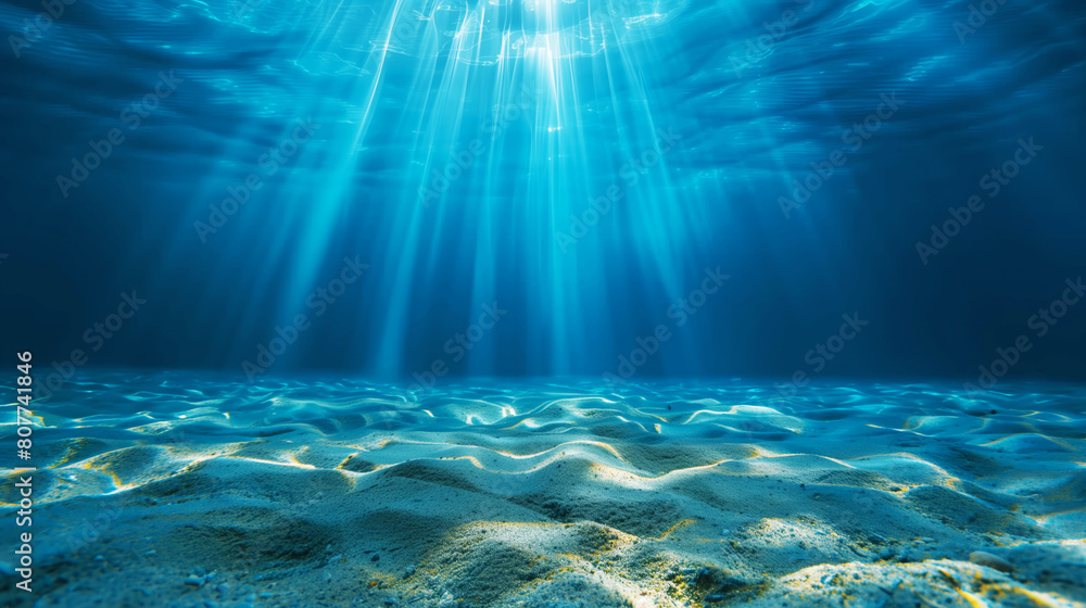 Obraz premium Underwater view showing the sandy ocean floor with rays of sunlight piercing through the blue water.