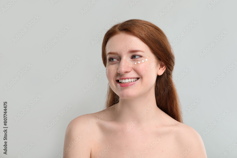 Smiling woman with freckles and cream on her face against grey background Smiling woman with freckles and cream on her face against grey background