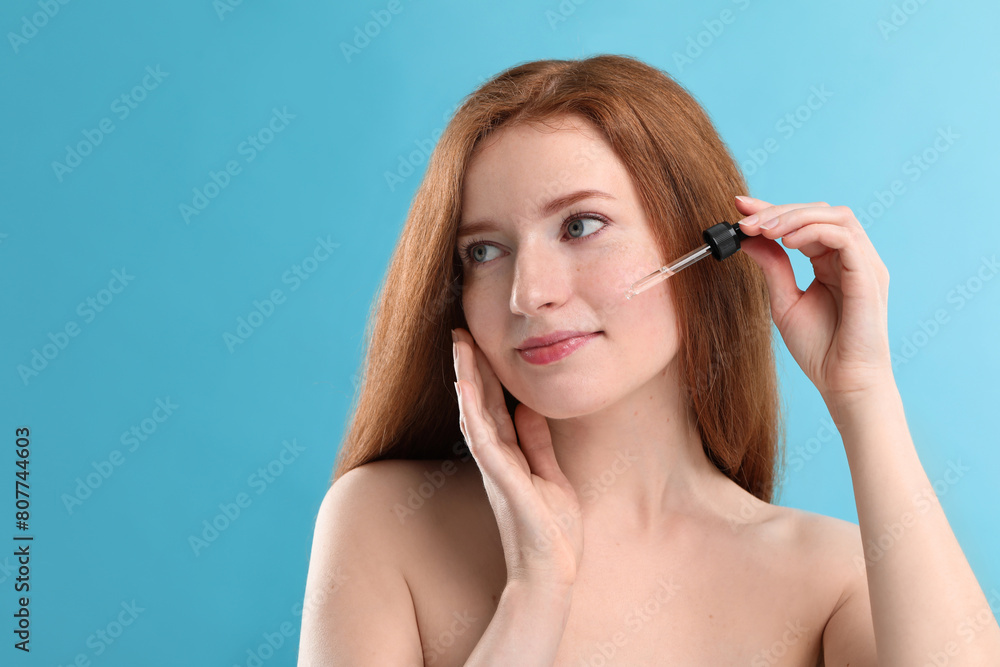 Beautiful woman with freckles applying cosmetic serum onto her face against light blue background. Space for text Beautiful woman with freckles applying cosmetic serum onto her face against light blue background. Space for text