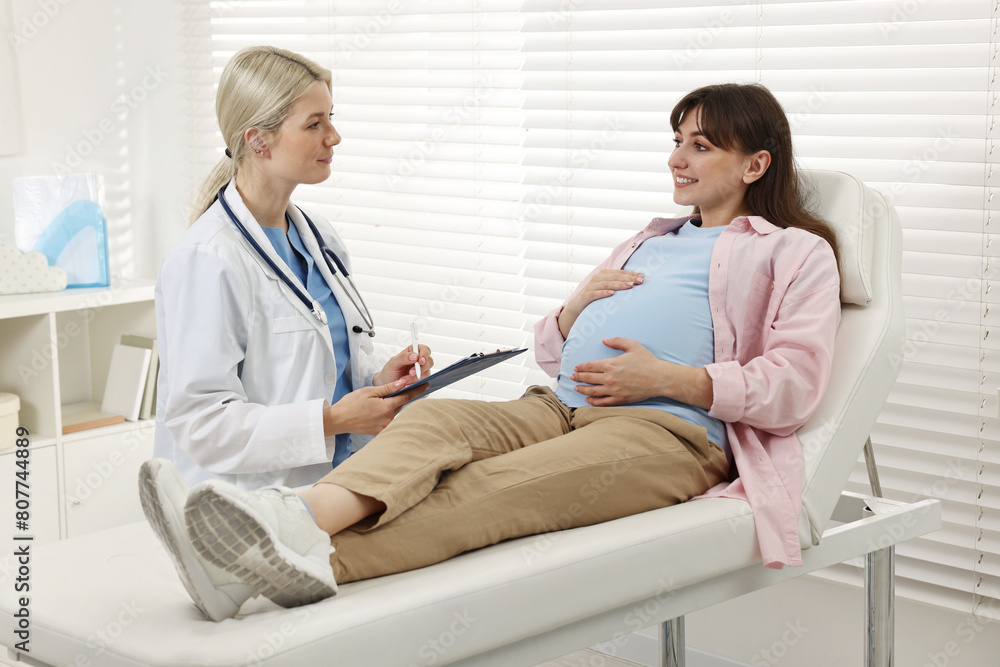 Doctor with clipboard consulting smiling pregnant patient in clinic Doctor with clipboard consulting smiling pregnant patient in clinic