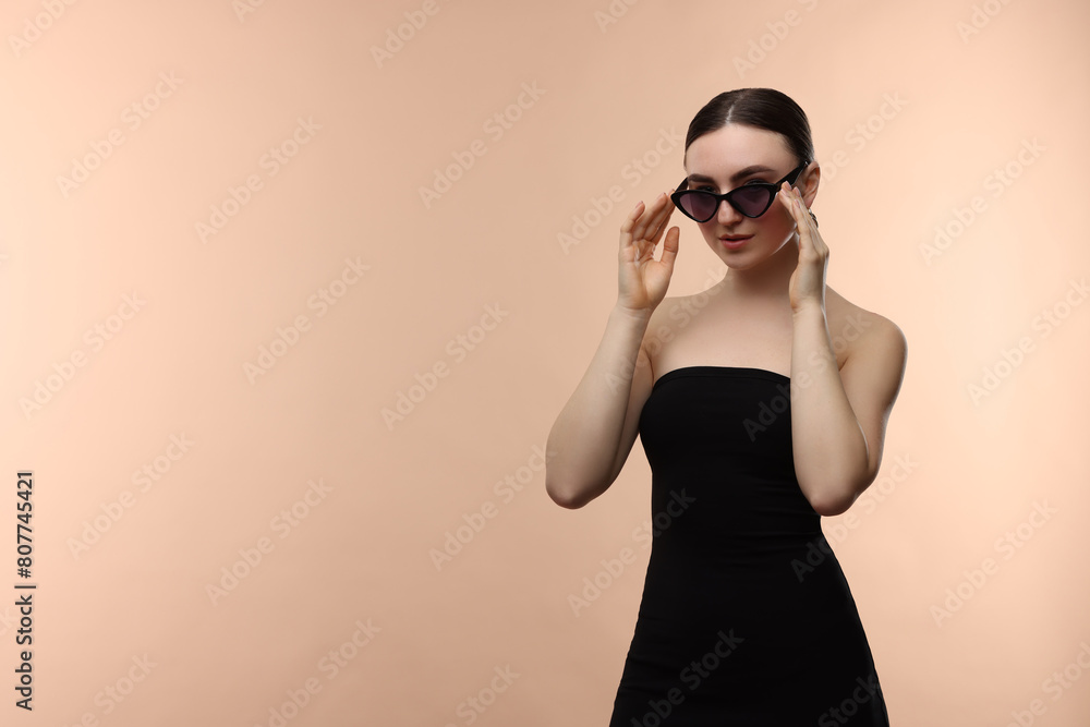 Fototapeta premium Portrait of beautiful young woman with sunglasses on beige background, space for text