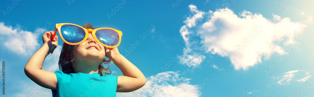 A little girl wearing big funny sunglasses enjoys the sun. Horizontal banner