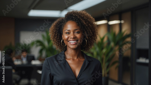 Bella donna di origini africane con capelli ricci sorride in un moderno ufficio con abito elegante photo