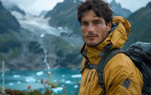 A man in a yellow jacket is standing in front of a mountain with a backpack on his back