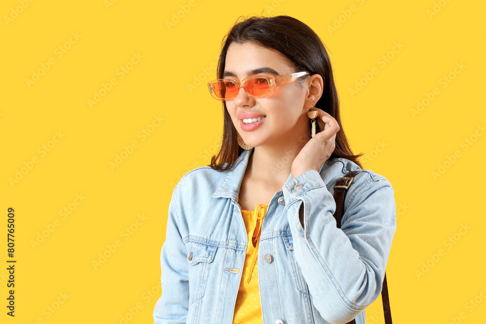 Beautiful young woman in stylish sunglasses on yellow background