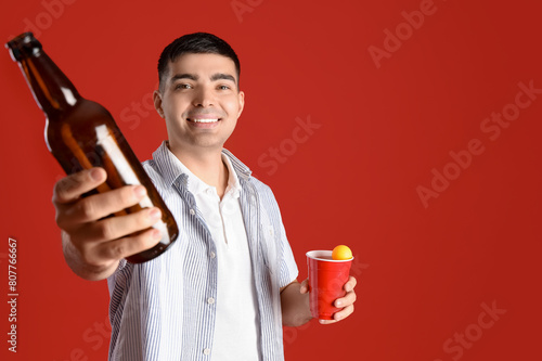 Young man with beer and ball on red background