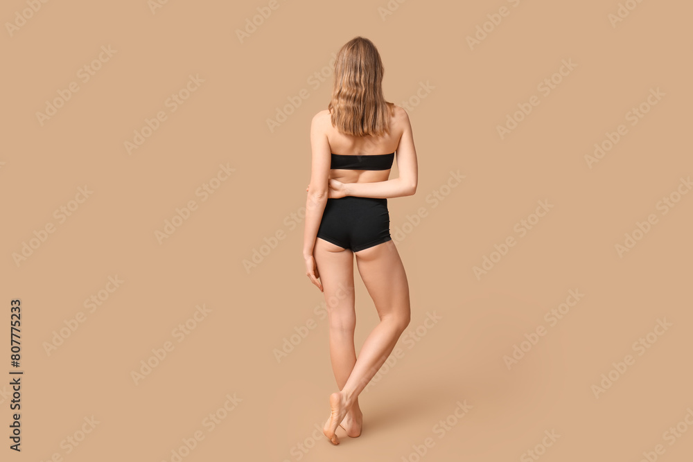 Attractive young woman in black underwear on beige background, back view Attractive young woman in black underwear on beige background, back view