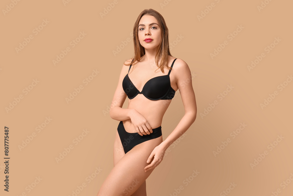 Fototapeta premium Sexy young woman in black underwear on beige background