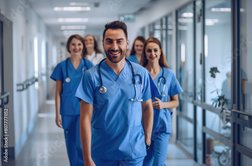 A group of happy male and female nurse in blue scrubs walking down the hospital hallway smiling at camera