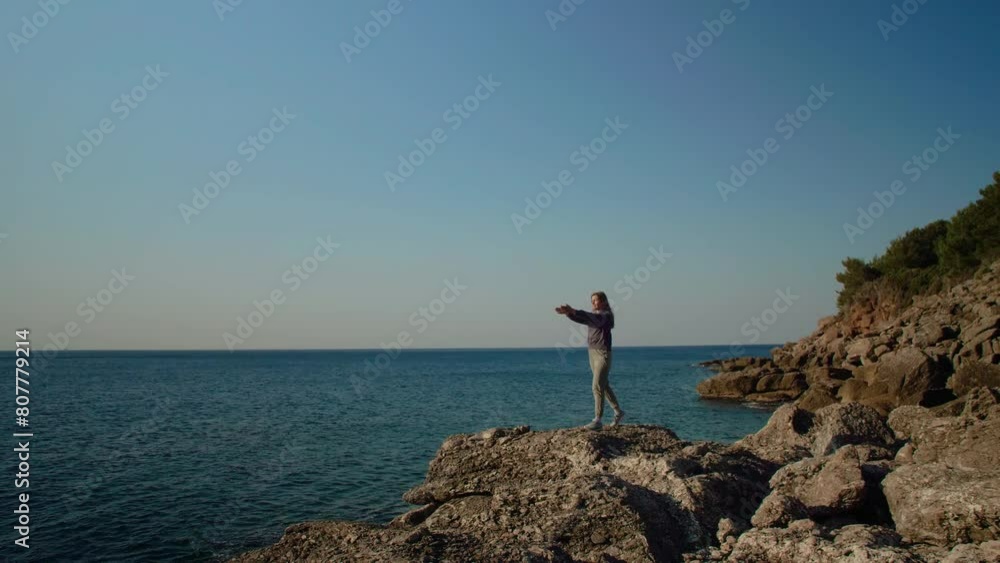A young woman standing on a rock by the sea doing exercises in the morning. A young woman standing on a rock by the sea doing exercises in the morning.