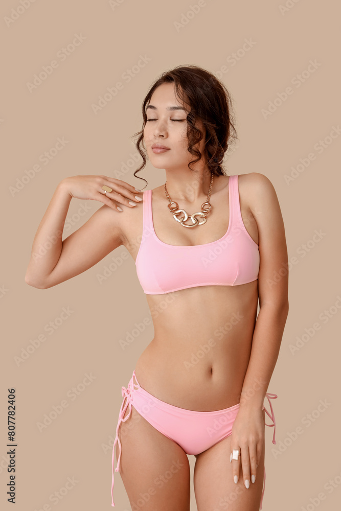 Naklejka premium Sexy young woman in pink swimsuit on beige background