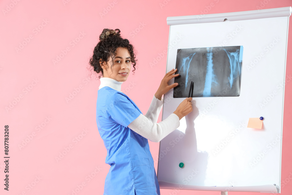 Female African-American medical intern with x-ray image on board against pink background Female African-American medical intern with x-ray image on board against pink background